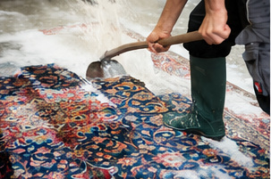 Person wäscht bunten Teppich mit Wasser und Bürste